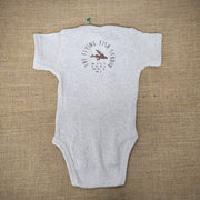An oatmeal baby onesie featuring a cartoon flying fish. The text "THE FLYING FISH STUDIO, WEST CAPE MAY NJ" is printed around & below the design.