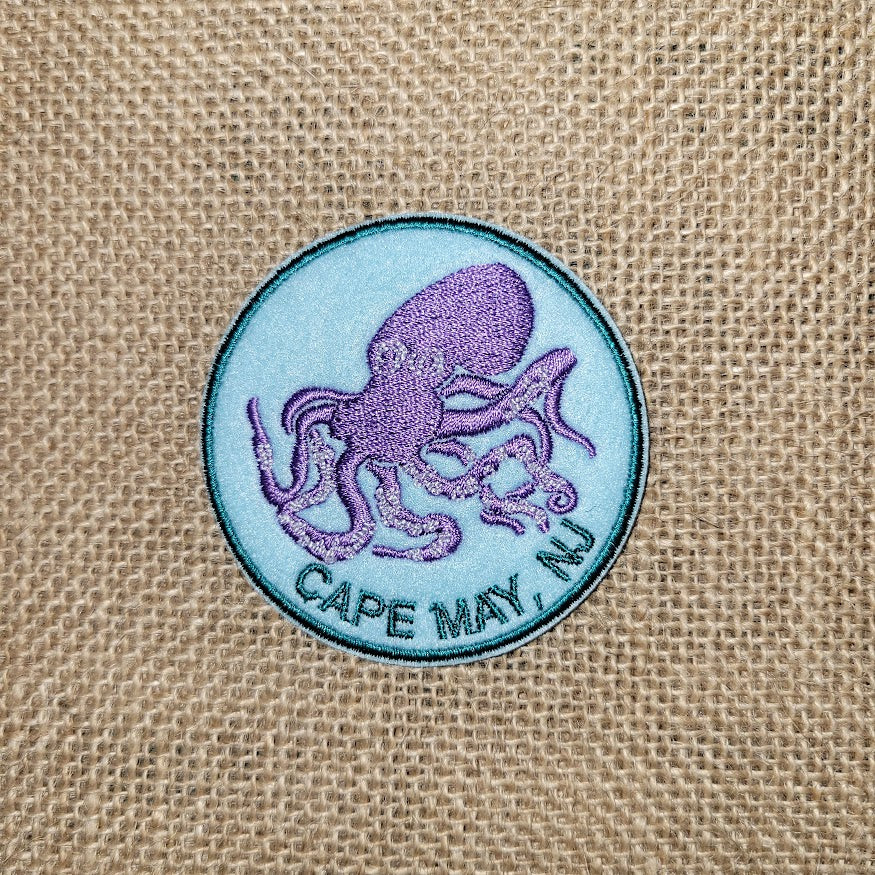 Blue iron-on patch with a graphic of a purple octopus and the words "Cape May, NJ" underneath it.