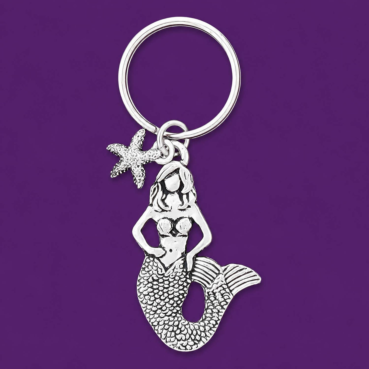 Silver mermaid keychain with starfish charm on a deep purple background.
