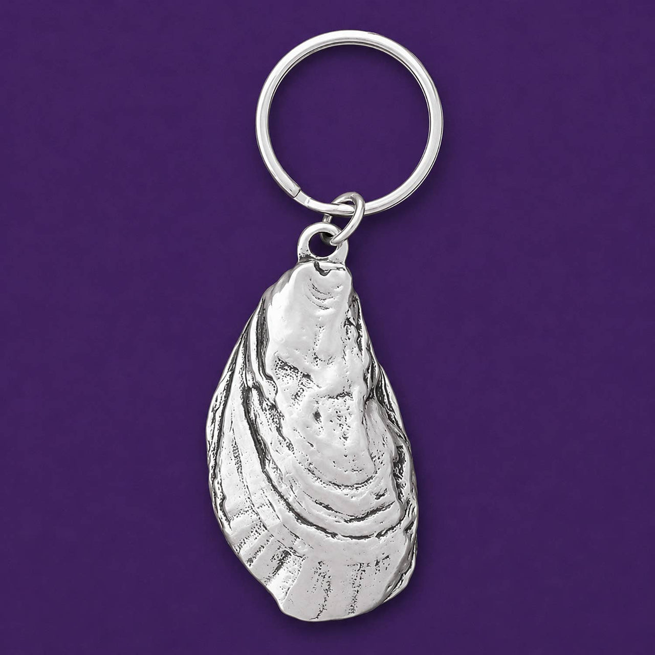Silver oyster shell keychain on a purple background.