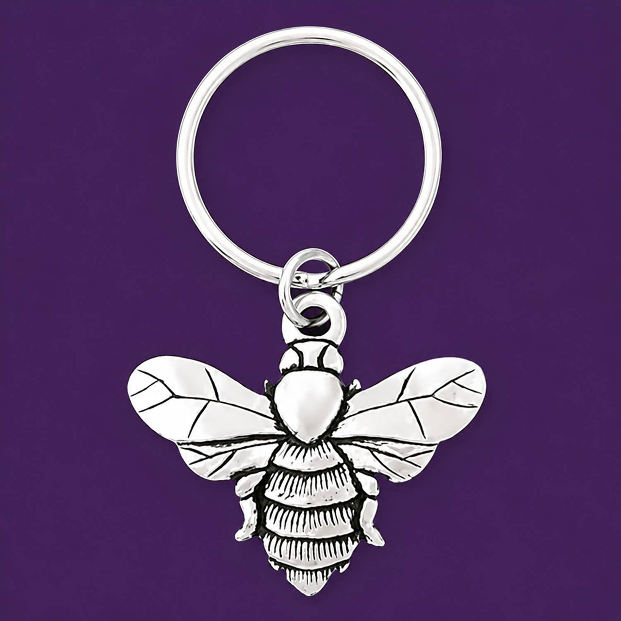 Silver bee keychain on a deep purple background.