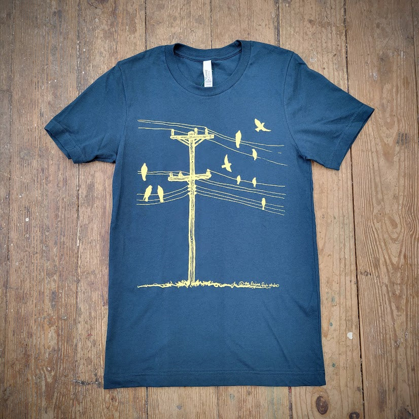 The front of a dark blue, short-sleeve T-shirt with a graphic of yellow birds on a wire, laid flat on a wooden surface.