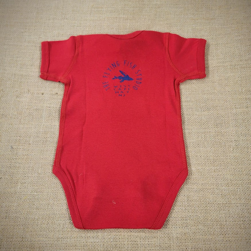 A red baby onesie featuring a cartoon flying fish. The text "THE FLYING FISH STUDIO, WEST CAPE MAY NJ" is printed around & below the design.