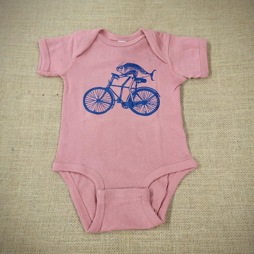 A mauve baby onesie with a graphic of a fish riding a bike.