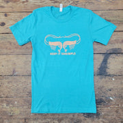 A turquoise t-shirt lies flat on a weathered wooden surface. The shirt features a graphic in a light orange color depicting two stylized shrimp facing away from each other, with their antennae curving upwards and outwards to almost touch. Below the shrimp, in a simple sans-serif font, are the words "KEEP IT SHRIMPLE". The wooden planks beneath the shirt are light brown with visible grain and some darker markings. A white tag is visible at the neckline of the t-shirt.