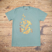 Green T-shirt with a graphic design of scattered butterflies on the front, printed with brown, yellow and orange ink. The shirt is laid flat on a wooden surface. 