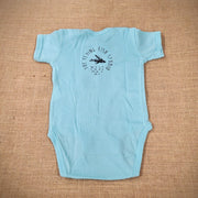 An aqua baby onesie featuring a cartoon flying fish. The text "THE FLYING FISH STUDIO, WEST CAPE MAY NJ" is printed around & below the design.