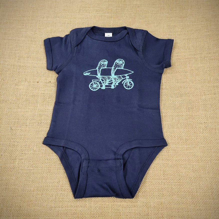 A navy baby onesie with a graphic of sloths riding a tandem with a surfboard.