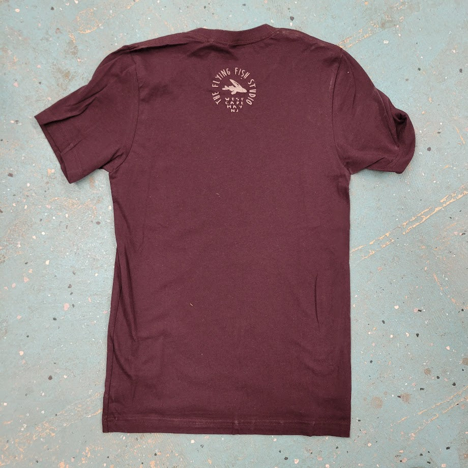 Maroon T-shirt with a logo on the back of the neck laid flat against a textured, blue background.