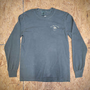 The front of a green long-sleeve T-shirt laid flat on a wooden surface. The 'Flying Fish Studio' logo is screen-printed on the left chest in a cream ink.