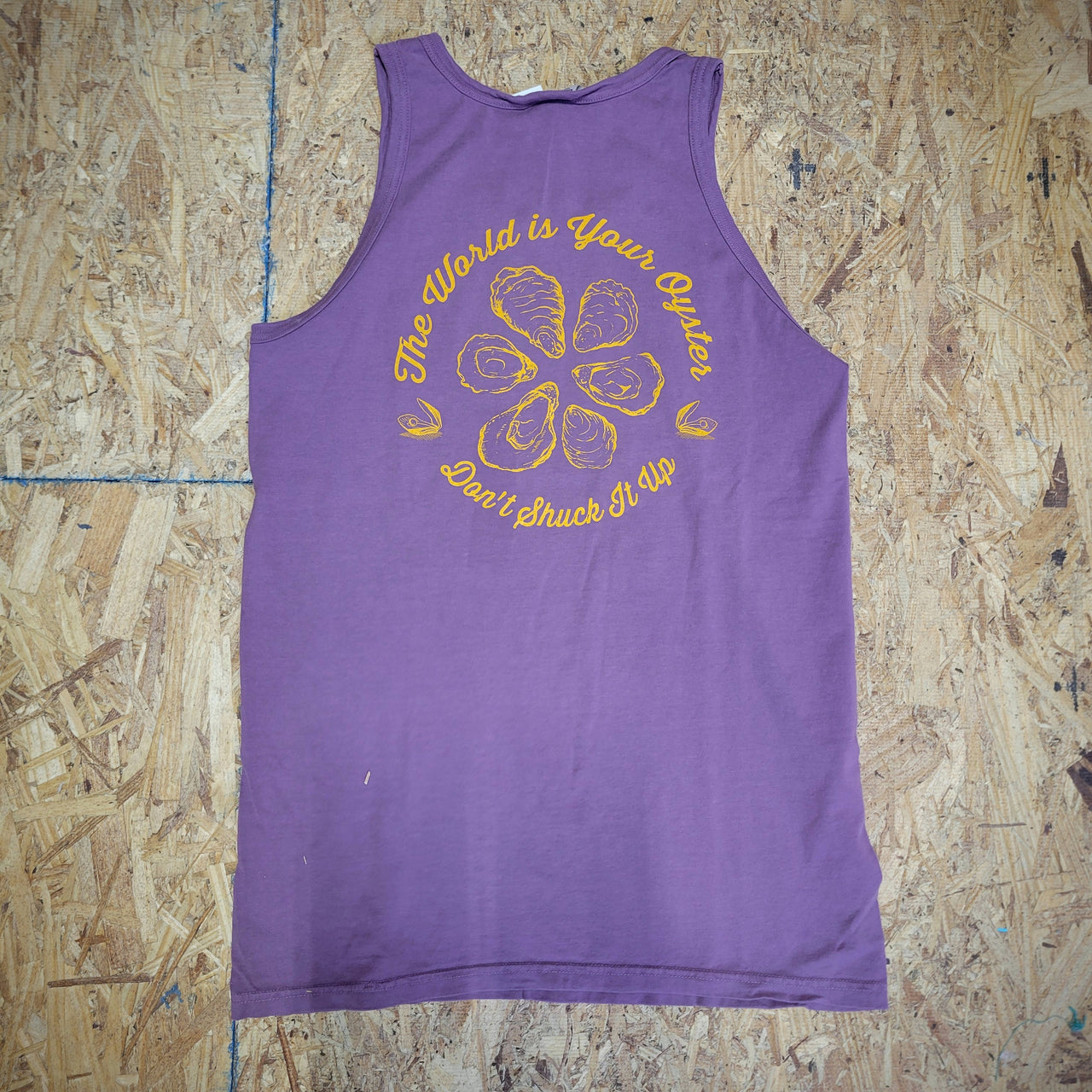 Back of a purple tank top with a design of oysters and text in orange ink. The text says 'The World is Your Oyster. Don't shuck it up.'