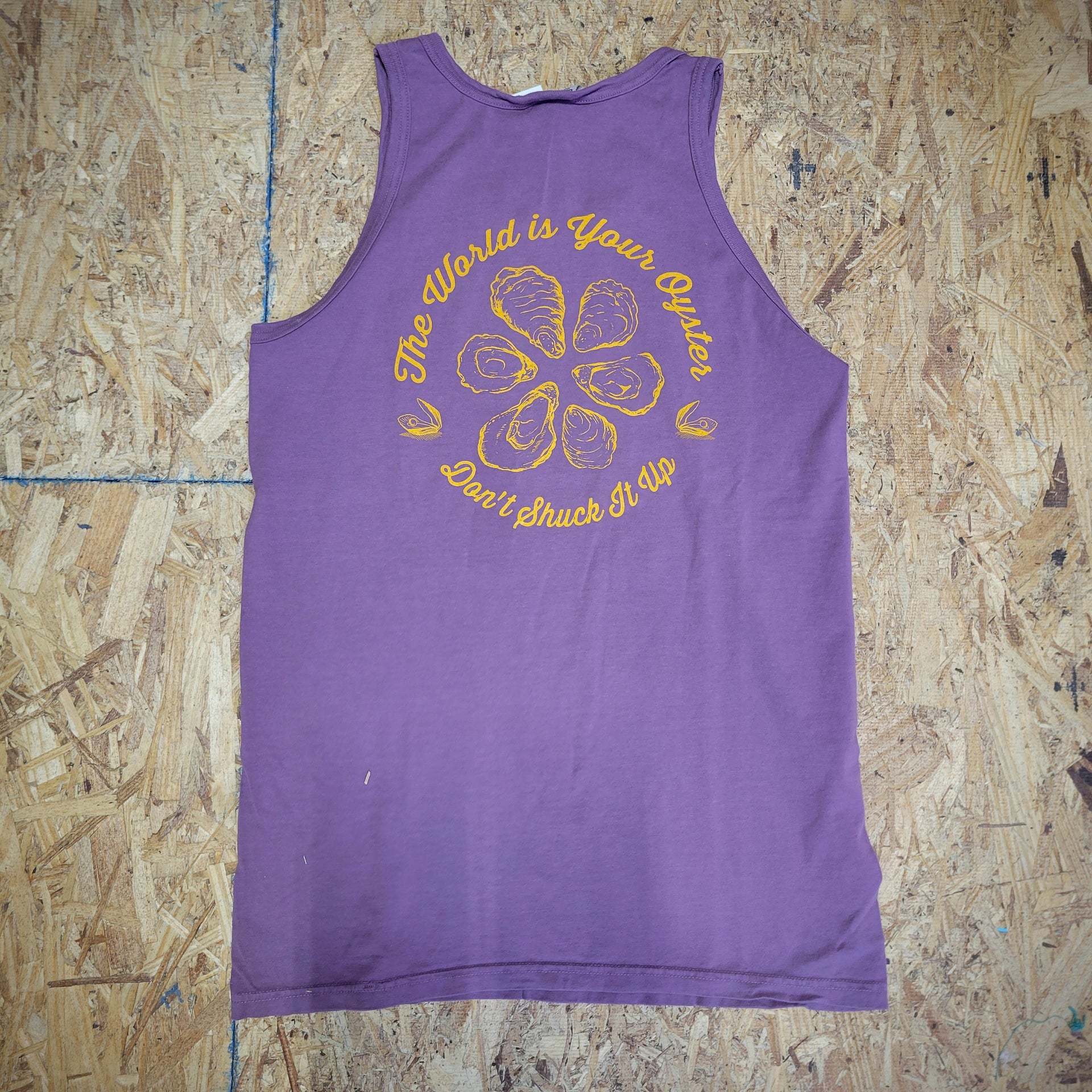 Back of a purple tank top with a design of oysters and text in orange ink. The text says 'The World is Your Oyster. Don't shuck it up.'