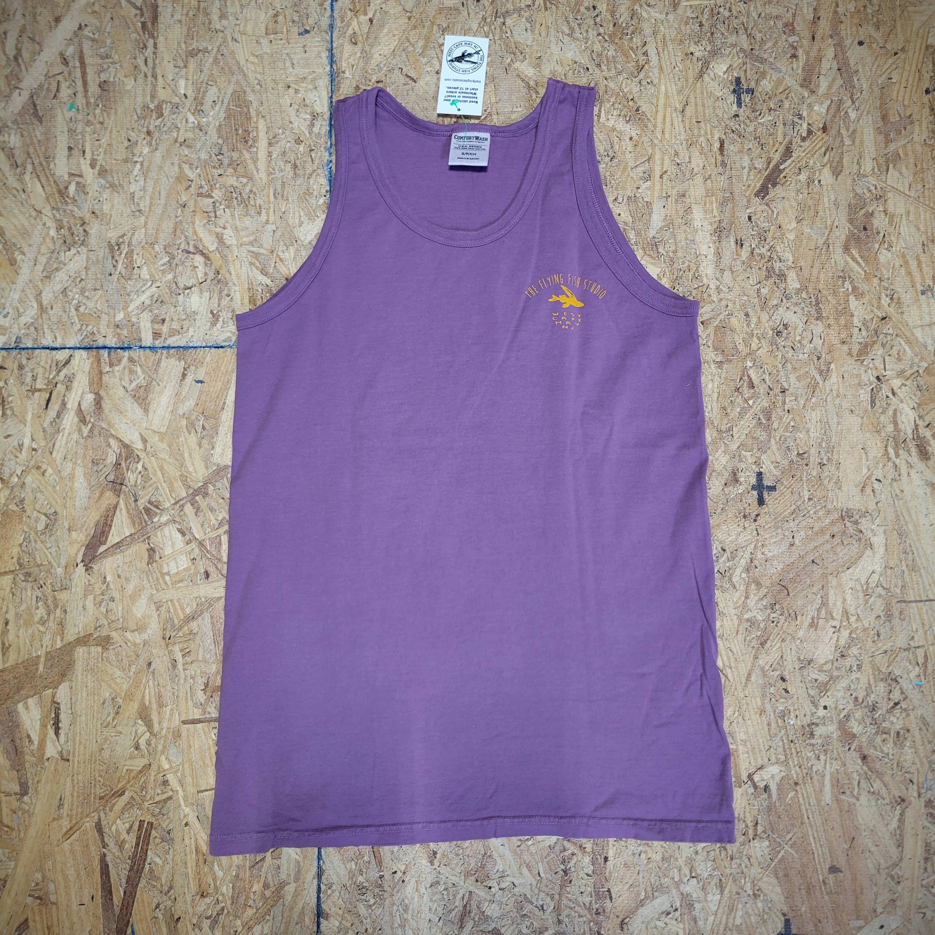 Purple tank top with the 'Flying Fish Studio' logo on the left chest in orange ink laid flat on a wooden background. 