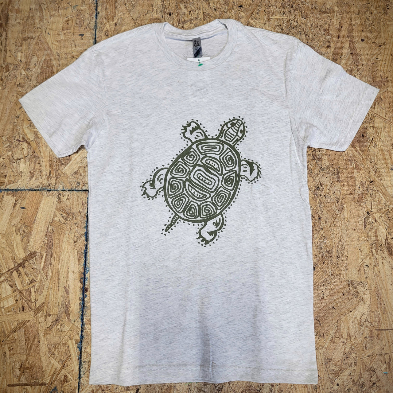 Gray, heathered T-shirt with a turtle design in green on the front, laid flat on a wooden surface.