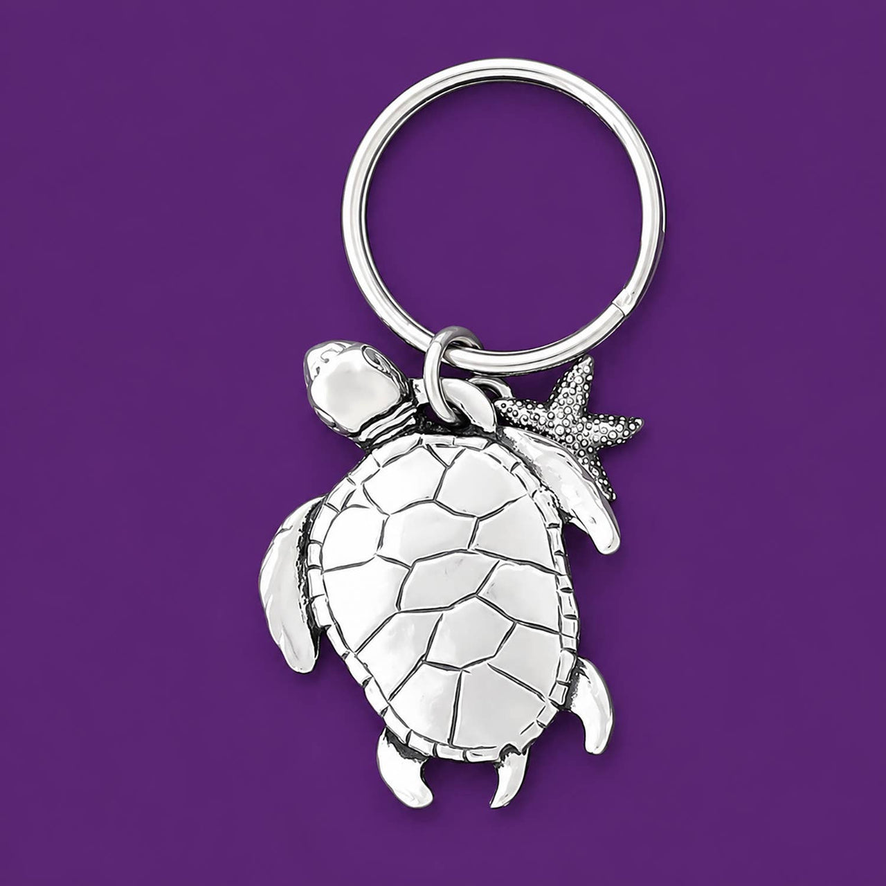 Silver turtle keychain with a starfish charm on a purple background.