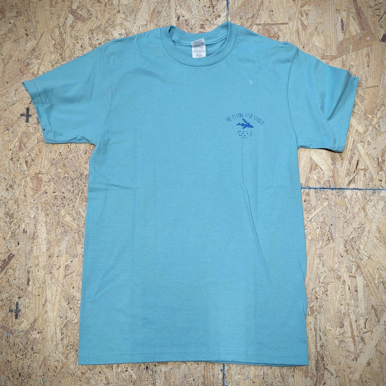 Greenish-blue T-shirt with the 'Flying Fish Studio' logo on the left chest on a wooden surface.