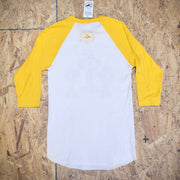 The back of a yellow and white baseball T-shirt laid flat on a wooden  surface. The 'Flying Fish Studio' logo is screen-printed on the back of the neck in yellow ink.