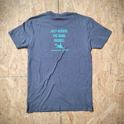 A blue T-shirt laid flat on a wooden surface with the words, "JUST ACROSS THE DANG BRIDGE."