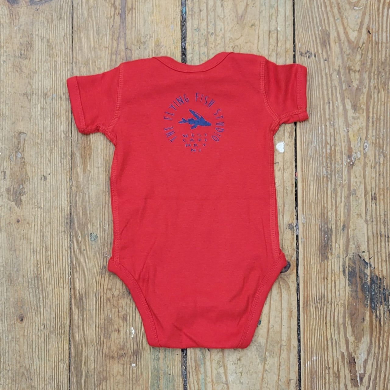 Bright red onesie featuring the 'Flying Fish' logo on the upper back in royal blue ink