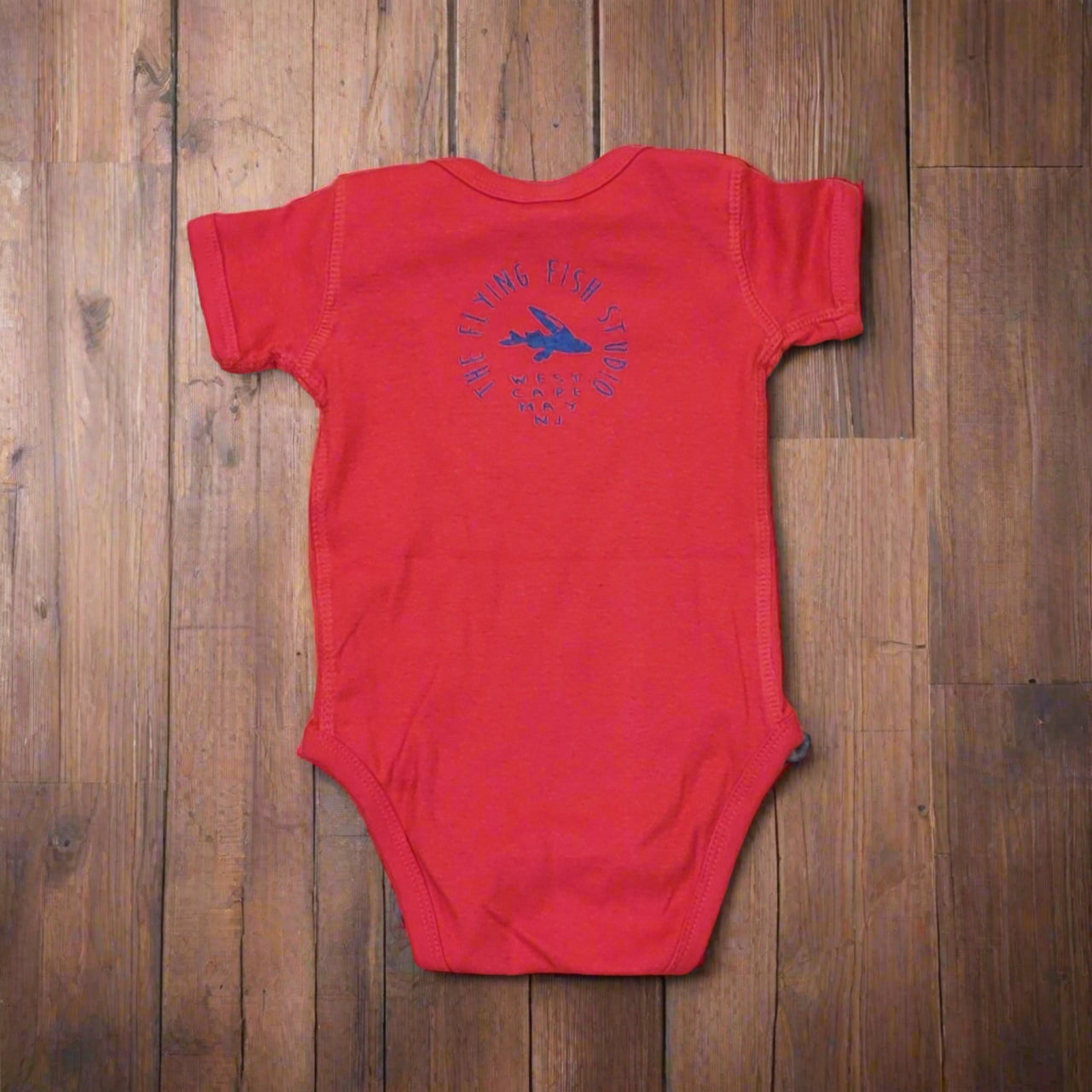 Bright red onesie featuring the 'Flying Fish' logo on the upper back in royal blue ink