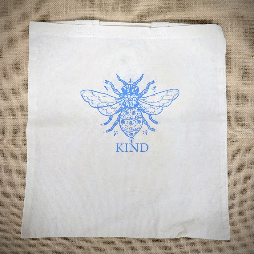 Natural, canvas tote bag with 'Bee Kind' design on the front in blue.