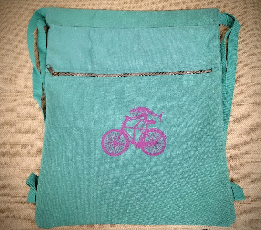 A seafoam blue drawstring bag with a purple fish o a bike on the front.
