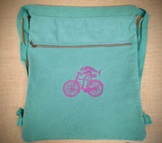 A seafoam blue drawstring bag with a purple fish o a bike on the front.