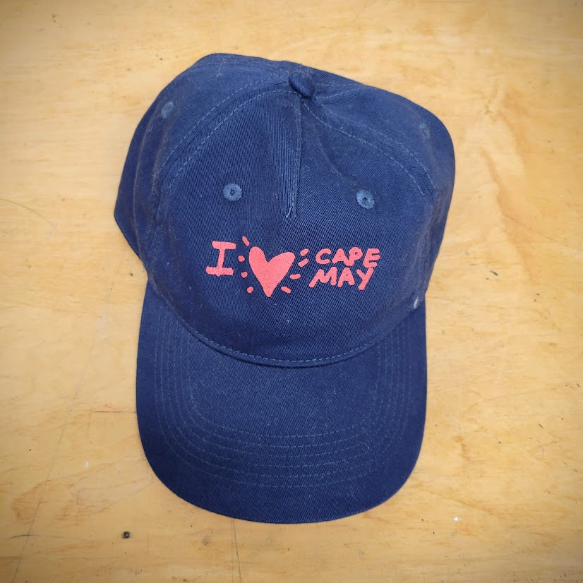 A navy, classic hat with 'I (heart) Cape May' on the front in red ink.