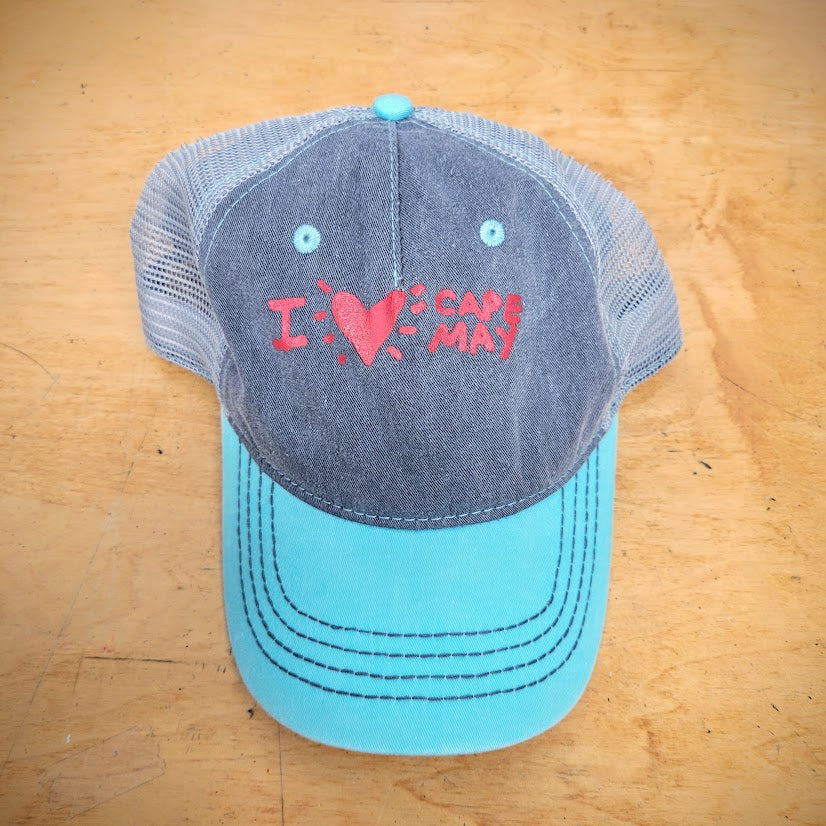 A grey and blue trucker hat with 'I (heart) Cape May' on the front in red ink.