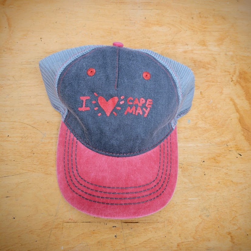 A red and grey trucker hat with 'I (heart) Cape May' on the front in red ink.