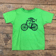 A green t-shirt featuring a fish on a bike on the front in navy ink.