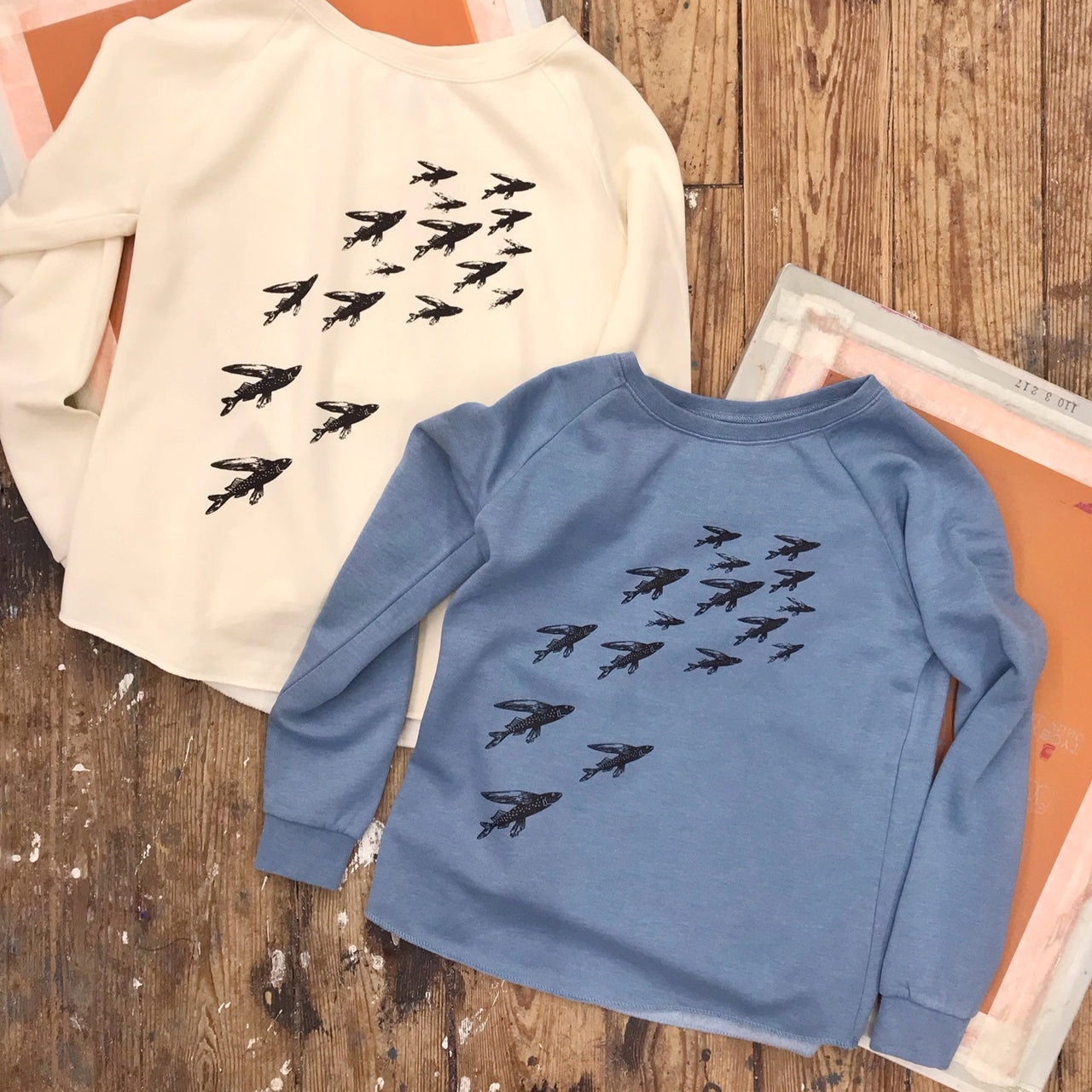 Two of the 'School of Fish' sweatshirts. One in bone cream and the other in misty blue.