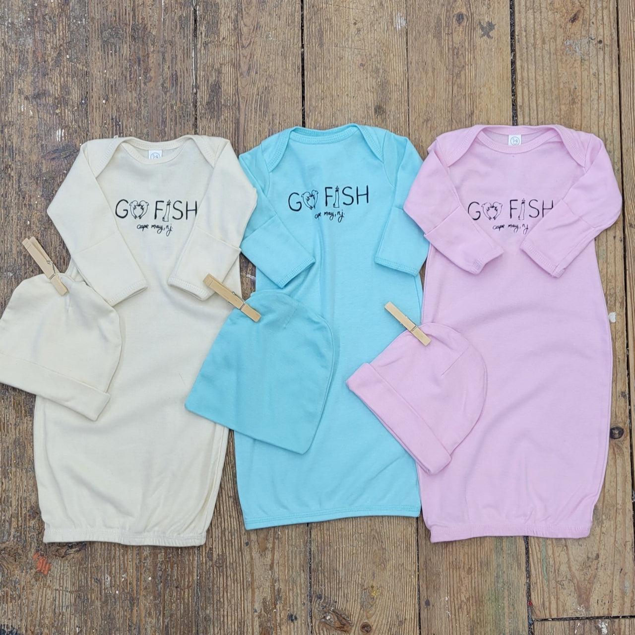 Three sets of baby layettes in cream, blue and pink featuring a 'Go fish! Cape May' design in black ink.