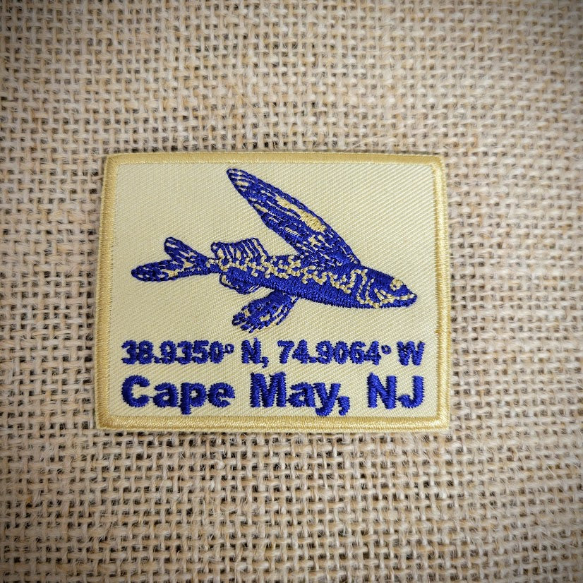 Rectangle, khaki patch featuring a blue flying fish, Cape May NJ, and its coordinates.