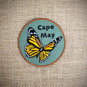 Round, brown-rimmed, green patch that says Cape May and features a monarch butterfly on the front.