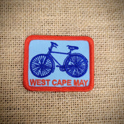 Rectangle, red-rimmed, blue patch featuring 'West Cape May' in red with a blue bike.