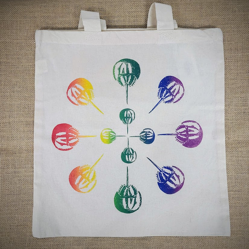 Natural, canvas tote bag with a multi-colored 'Horseshoe Crab' mandala screen-printed on the front.