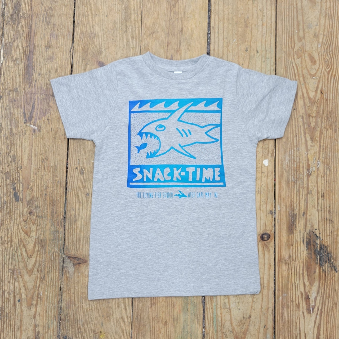 A grey t-shirt with a shark design on the front and the words, 'snack-time.'