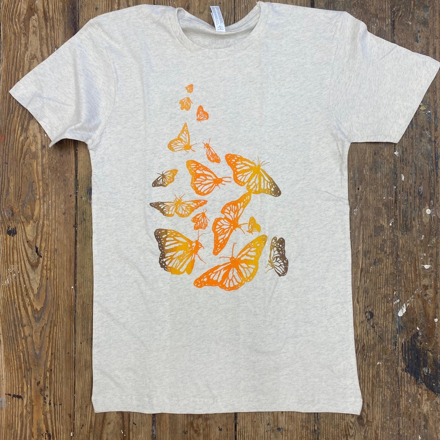 A heather greyish-cream shirt monarch butterflies on the front in gradient ink.