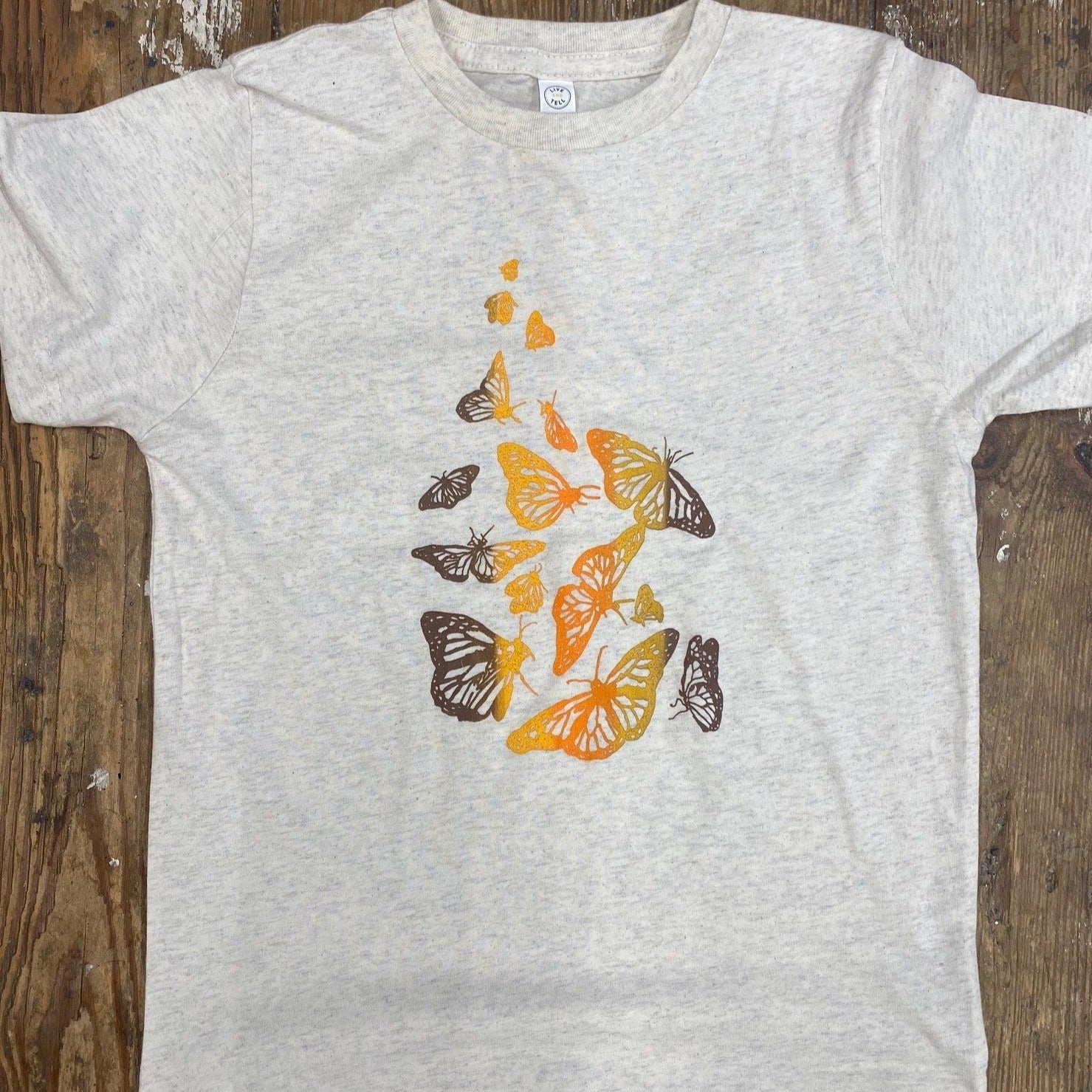 A heather cream t-shirt with monarch butterflies on the front.