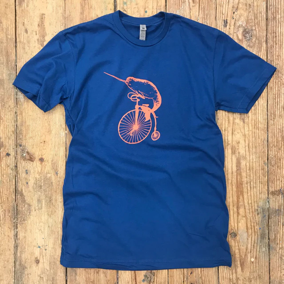 A blue t-shirt with the 'Narwhal on a Penny-farthing' design on the front with orange ink.